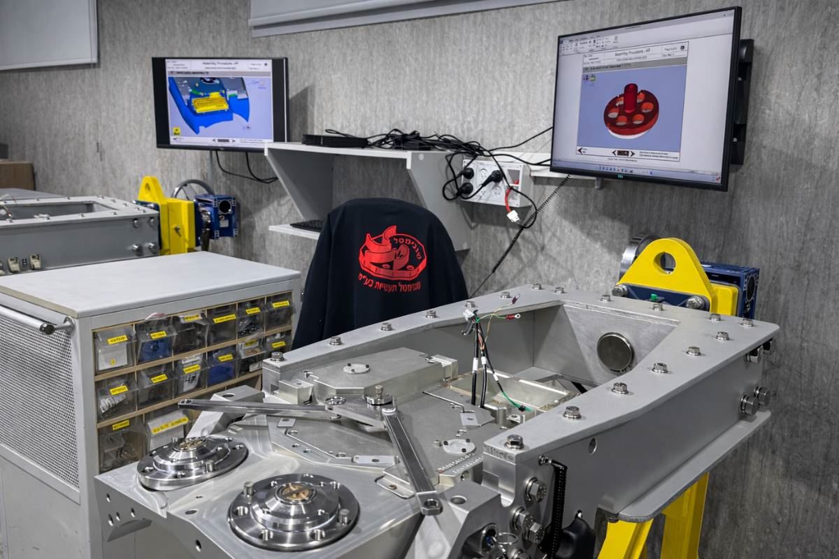 Large mechanical assembly beside CAD models on screens